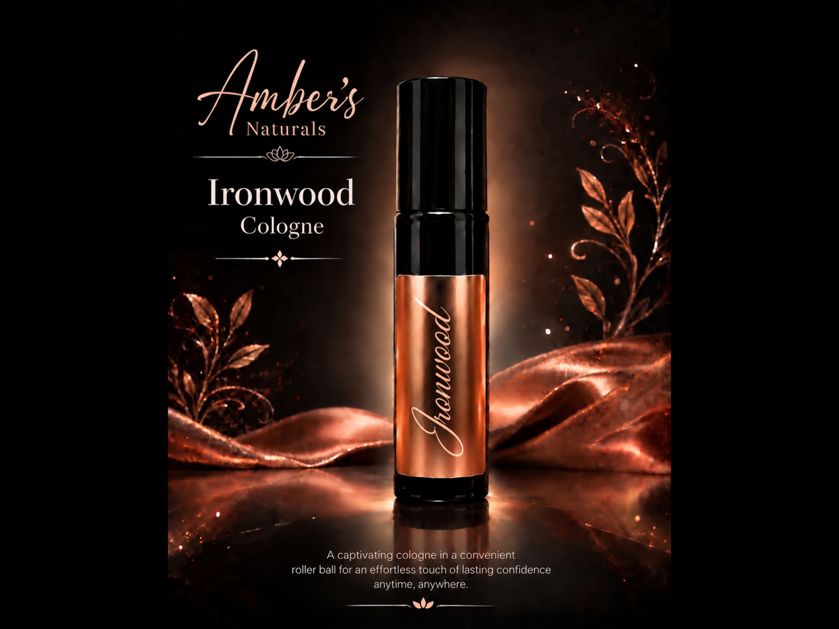 A bottle of Amber's Naturals Ironwood Cologne stands upright on a reflective surface against a dark background with warm copper-toned fabric and decorative leaf graphics. The bottle has a black cap and a metallic copper body with the brand name written in white script.