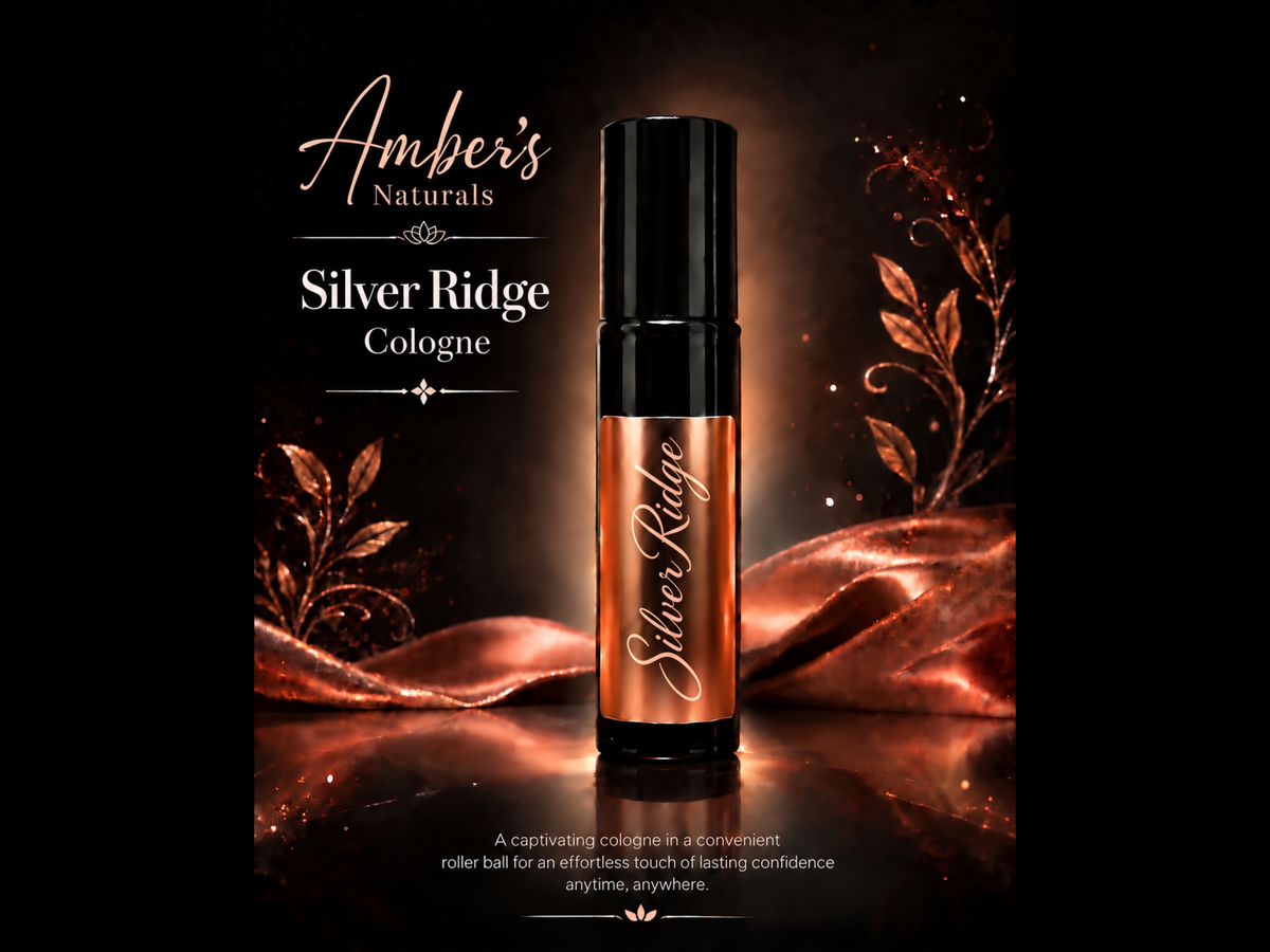 A bottle of Amber's Naturals Silver Ridge Cologne stands upright on a reflective surface against a dark background with warm copper-toned decorative leaves and draped fabric. The brand text 'Amber's Naturals' and product name 'Silver Ridge Cologne' appear above.